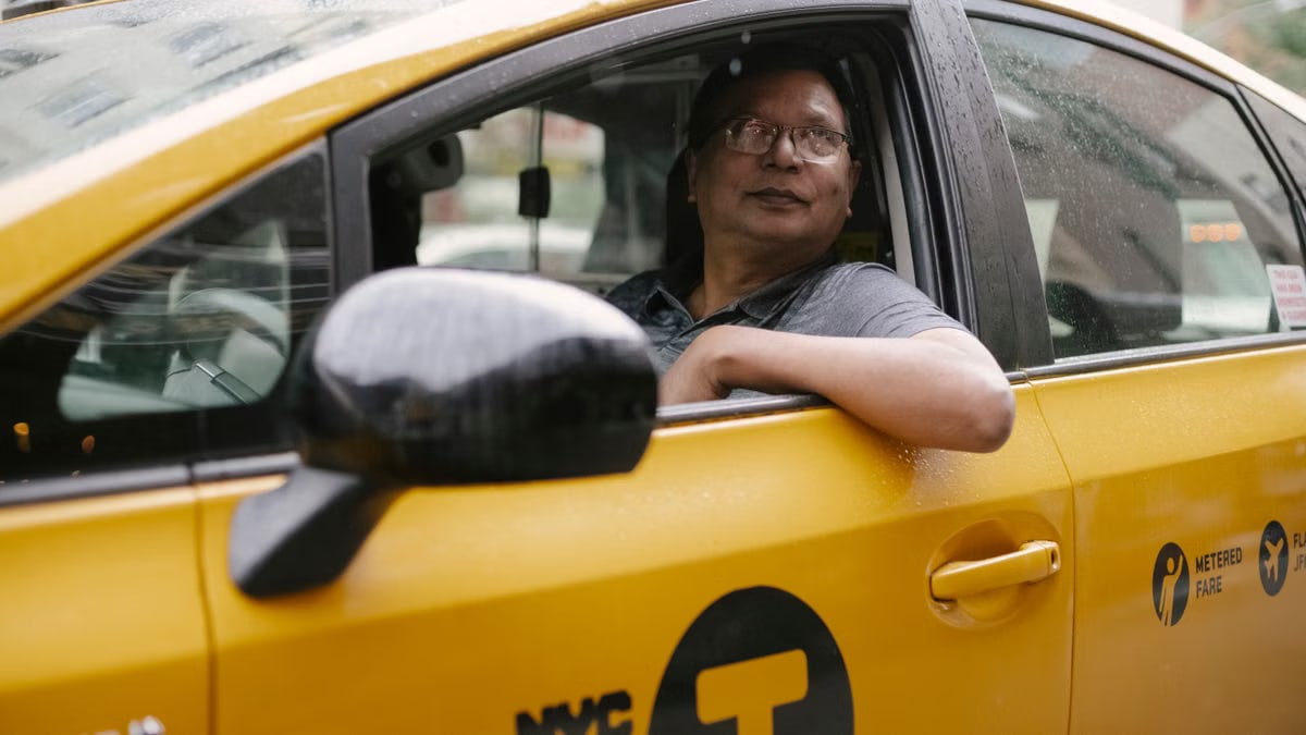 Serious taxi driver in glasses sitting in yellow automobile and looking up on street in city in daytime